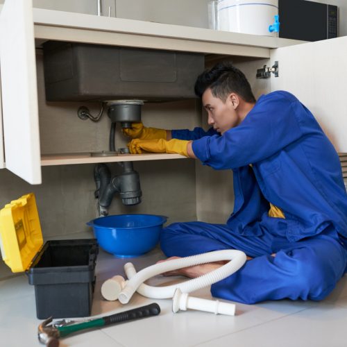 asian plumber blue overalls clearing blockage drain